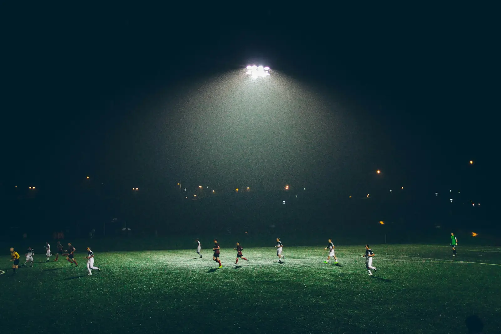 Partido de fútbol nocturno bajo un foco en un campo iluminado