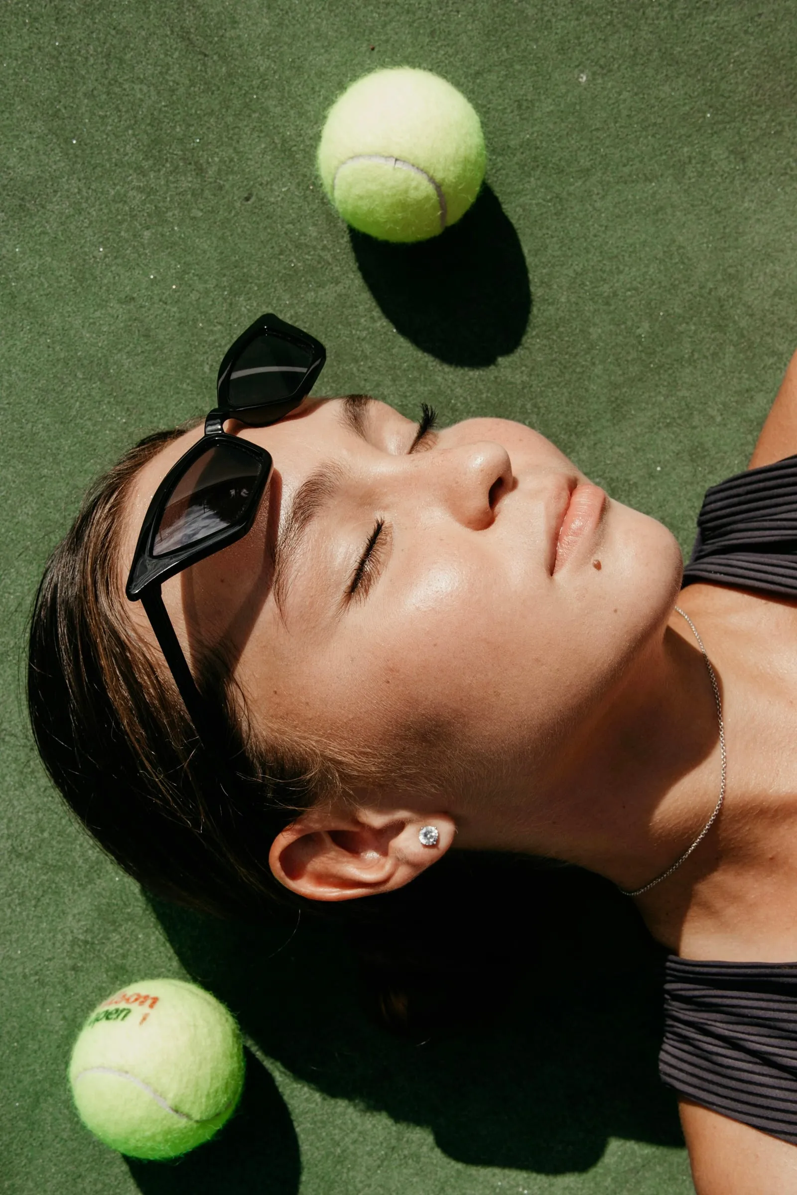 Tenista descansando tumbada en la pista con los ojos cerrados, junto a dos pelotas